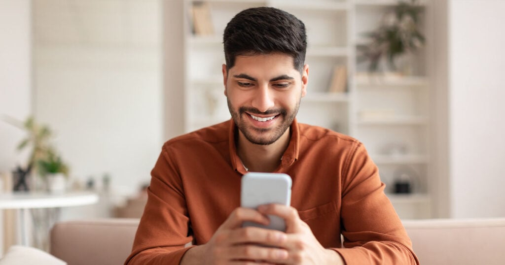 Portrait of smiling Arab man using smartphone at home stock photo_social
