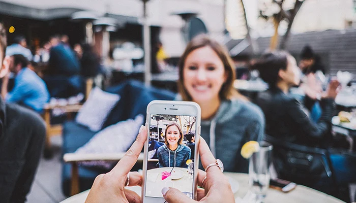 Person holding cell phone taking a photograph of smiling girl at restaurant table