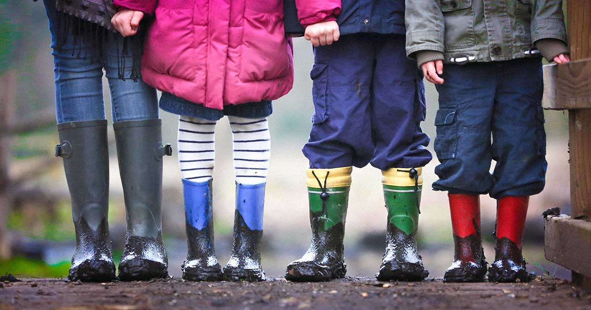 Four young kids lined up wearing dirty rubber boots.