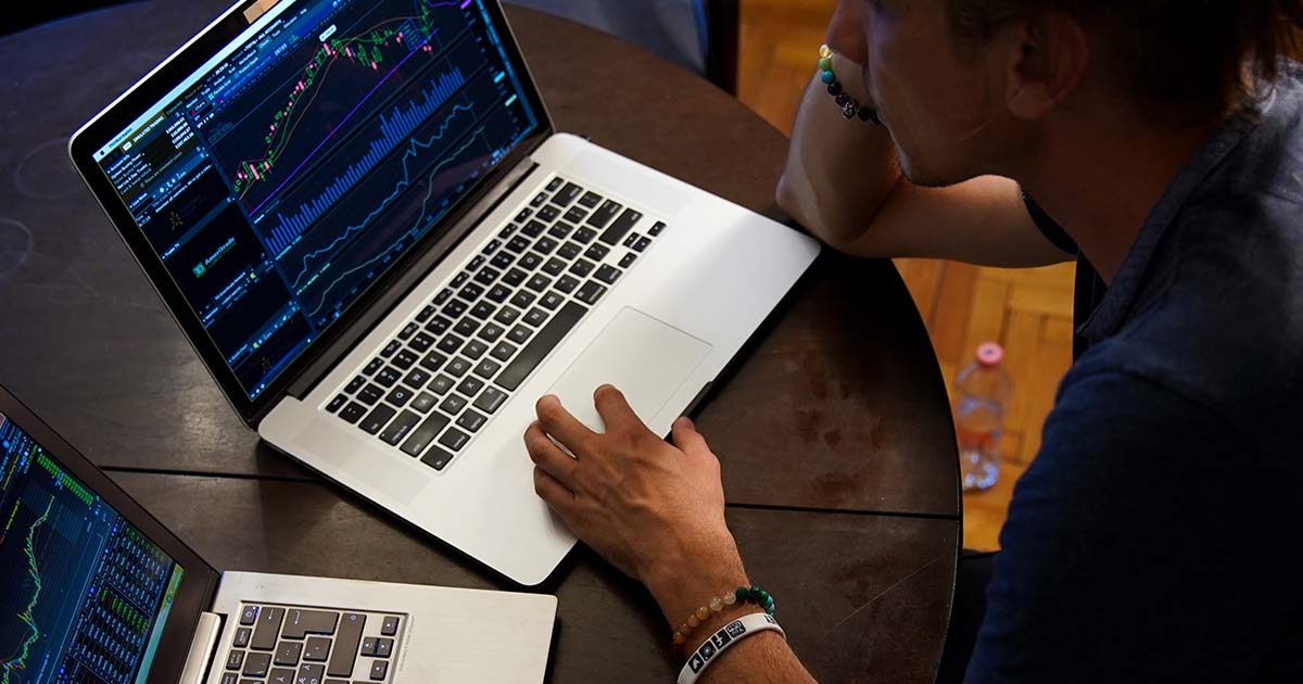 Man sitting in front of two laptops looking at stocks