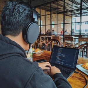 man sitting in front of laptop with headphones on in cafe