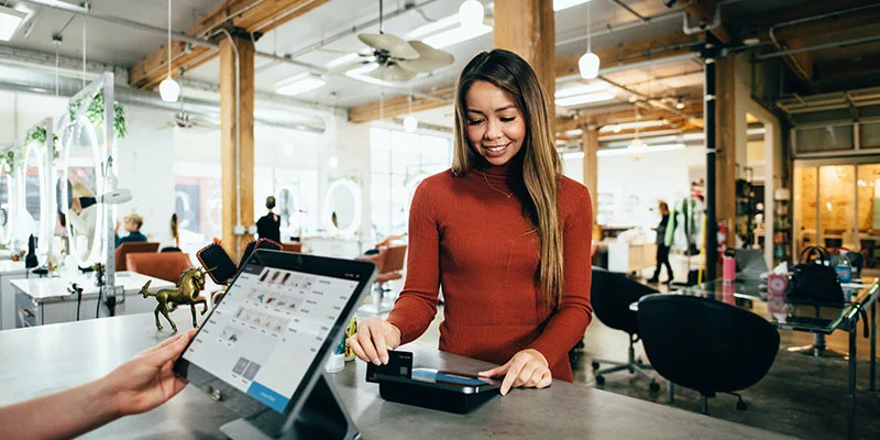 Young woman in red sweater making payment in-store with credit card