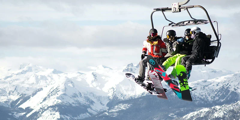 Four friends with winter gear and snowboards on chairlift at Whistler