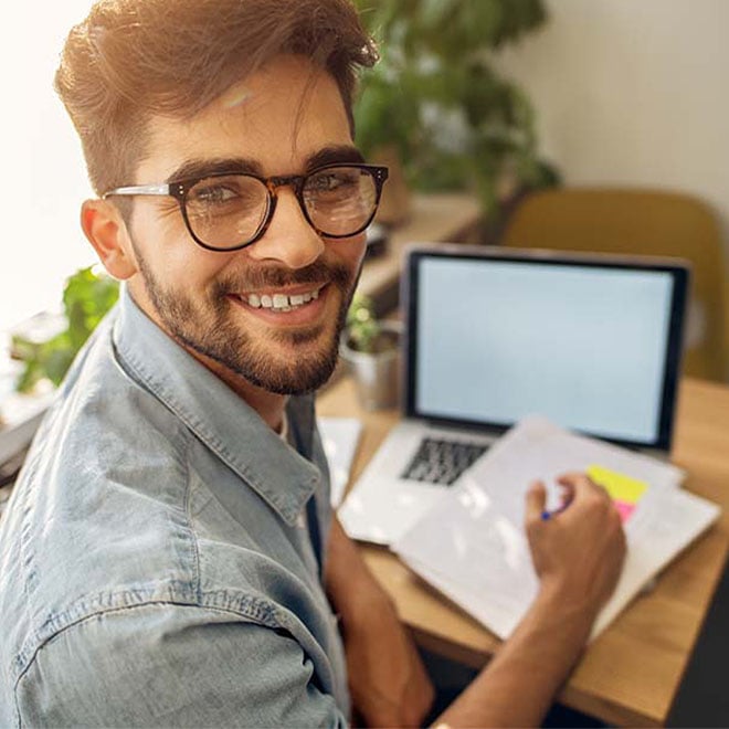 young man smiling sitting at desk with laptop