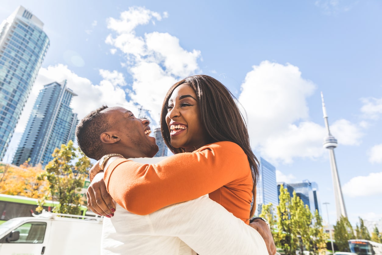 Couple hugging and laughing. The Toronto skyline is visible in the background.