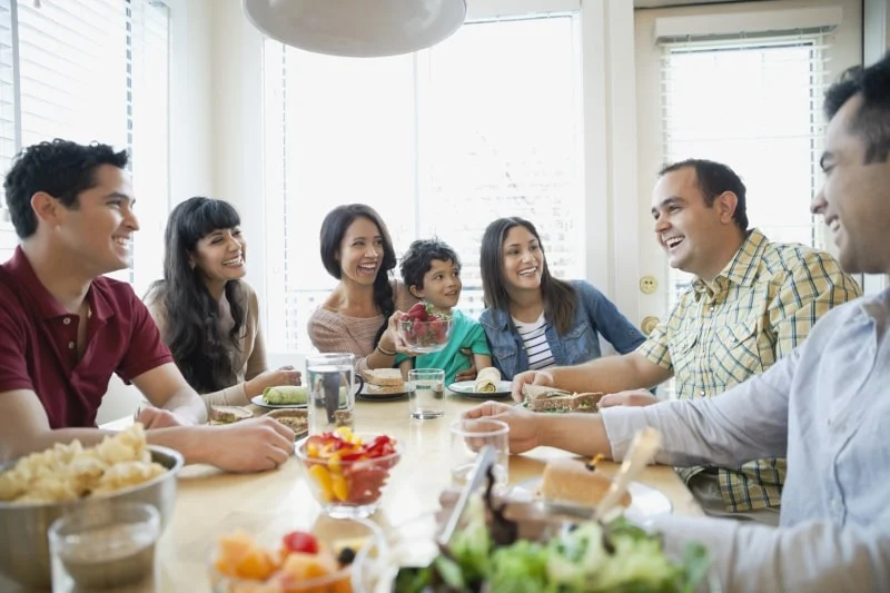 A family sits around a table, sharing a meal, smiling and laughing