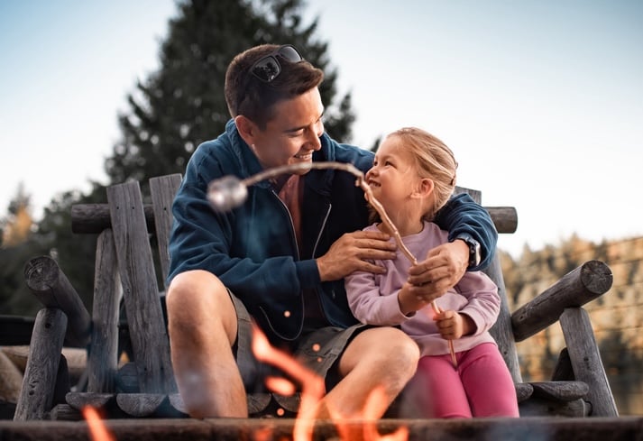 Father spending fun time with his little daughter roasting marshmallows over a campfire enjoying outdoor activity.
