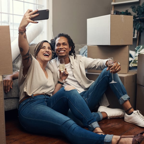 Young happy couple sitting on the floor celebrating their move into a rental apartment surrounded by moving boxes