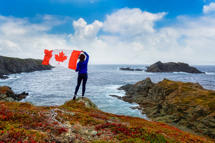 Adventurous woman holding a Canadian Flag on a Rocky Atlantic Ocean Coast