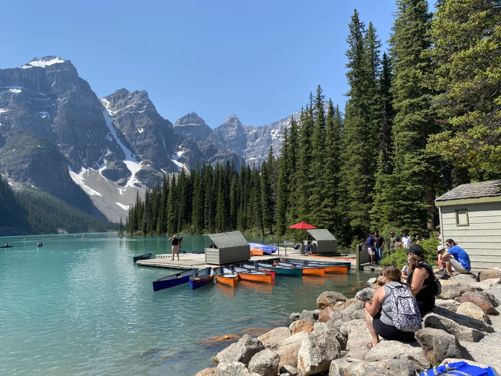 Your Ultimate Canadian Travel Bucket List awaits, featuring Lake Louise in Alberta .Turquoise waters surrounded by towering snow-capped mountains and lush pine forests.