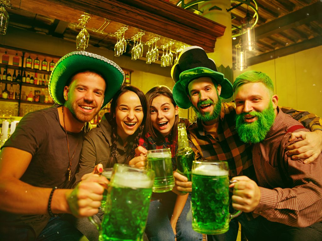 Five friends celebrating St. Patrick’s Day in a lively pub, all dressed in festive green attire.