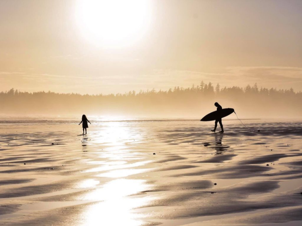 Tofino at sunset with surfers silhouetted against the golden-orange sky