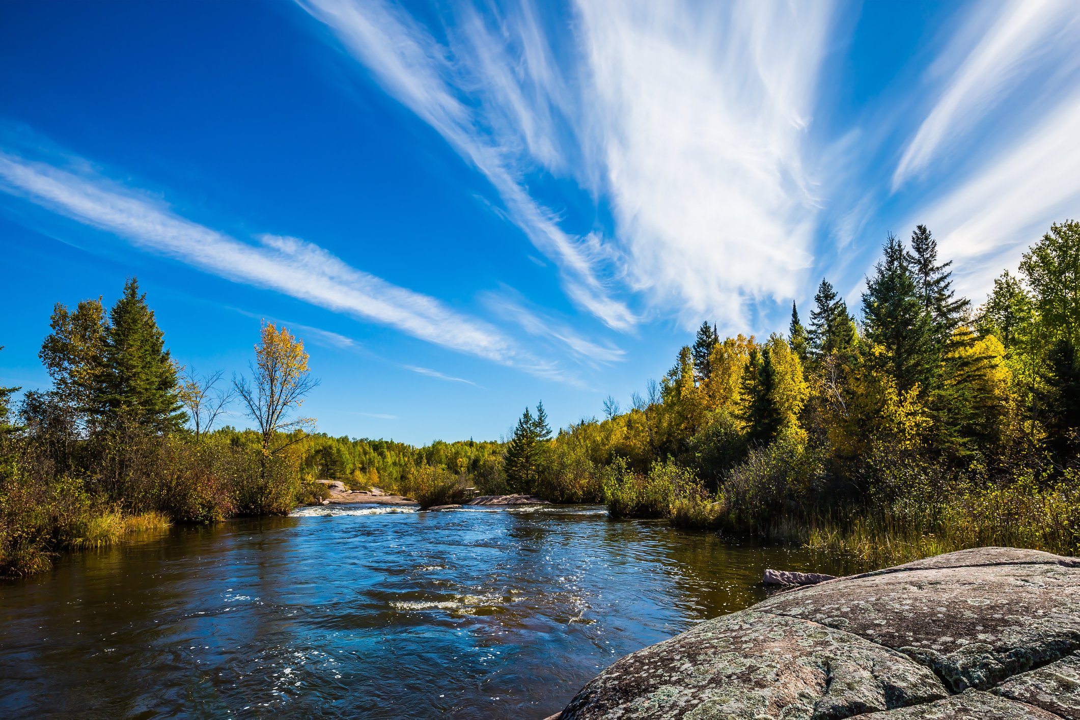 Tranquil landscape in the Old Pinawa Dam Park. Thin cirrus clouds and foam on the Winnipeg River. Trend of travel "Around the World"