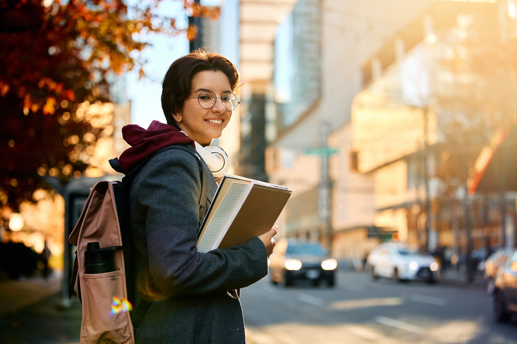 Young happy female student standing on the street and looking at camera.