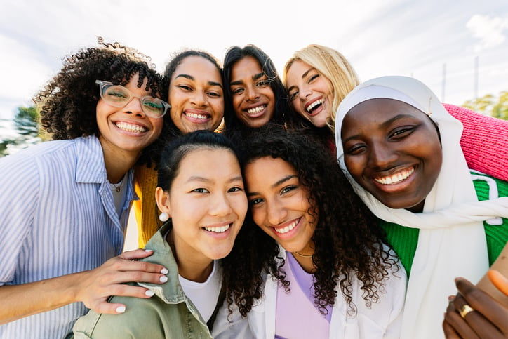 Group portrait of happy diverse women standing together outdoors. Millennial female friends from different cultures smiling at camera. Friendship and youth community concept.