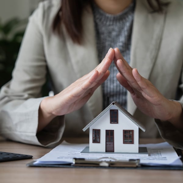 Businesswoman sitting in front of a model home sitting on home insurance policy paperwork on a clipboard