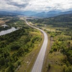 A breathtaking aerial perspective of a peaceful road meandering through verdant forests and gentle hills in Alberta, Canada, capturing the essence of nature and serenity.
